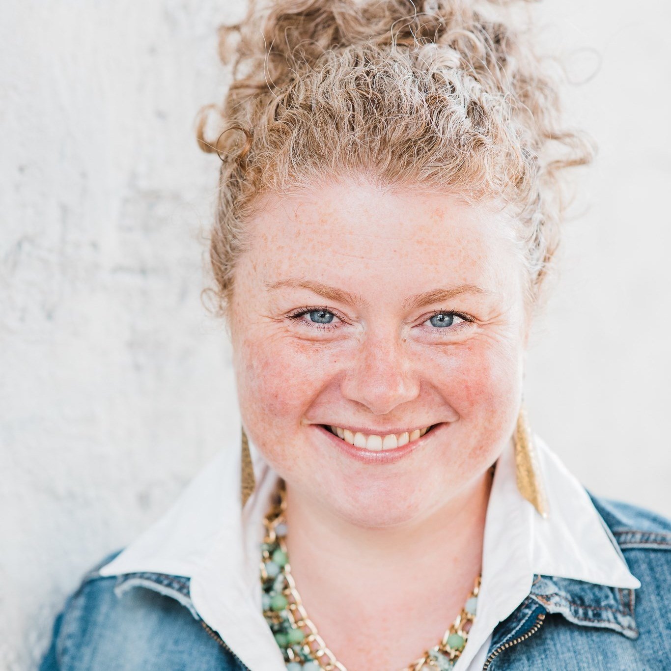 Portrait photo of a smiling woman with wavy hair in a denim jacket